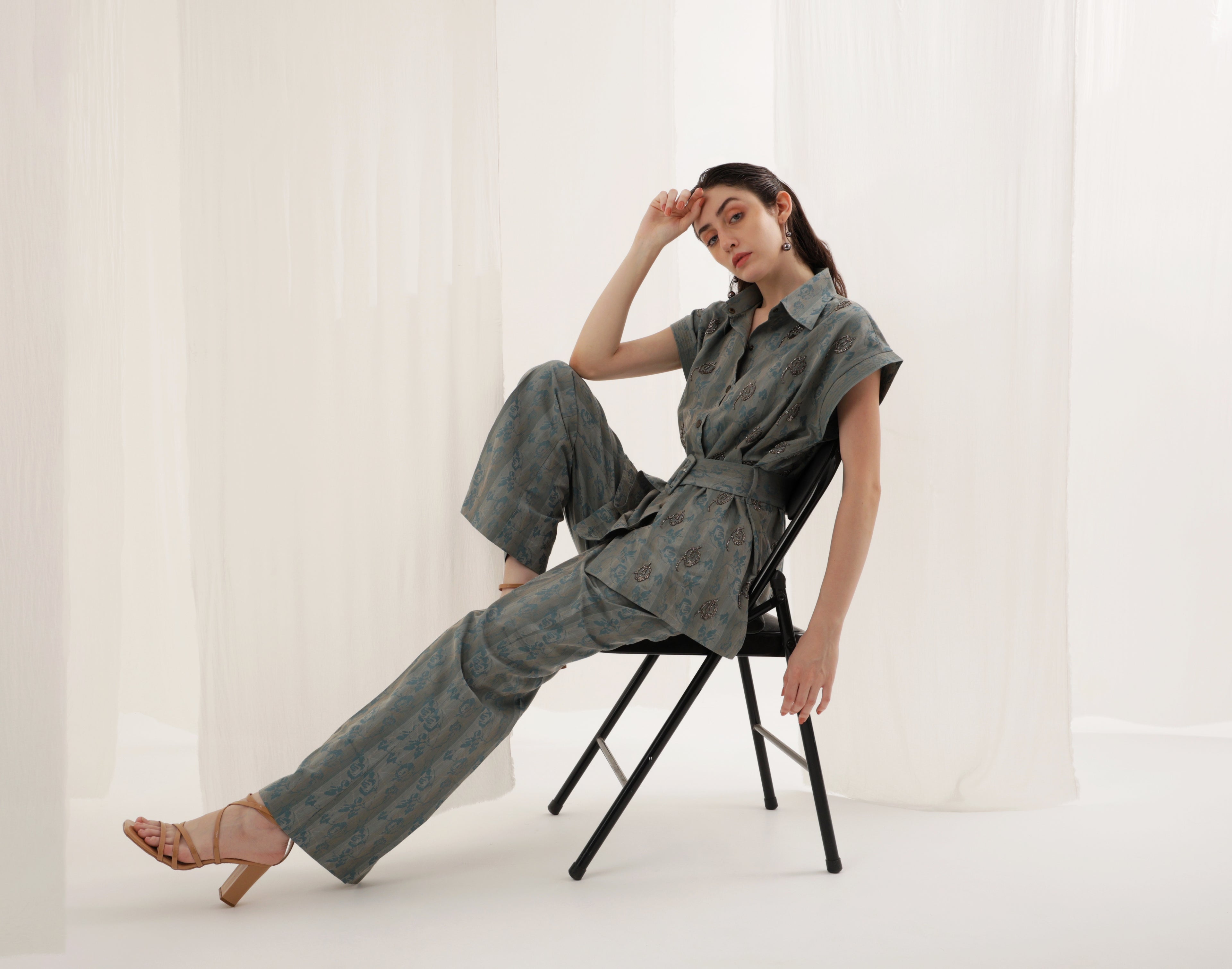 Woman sitting on a chair wearing a gray jumpsuit against a white background